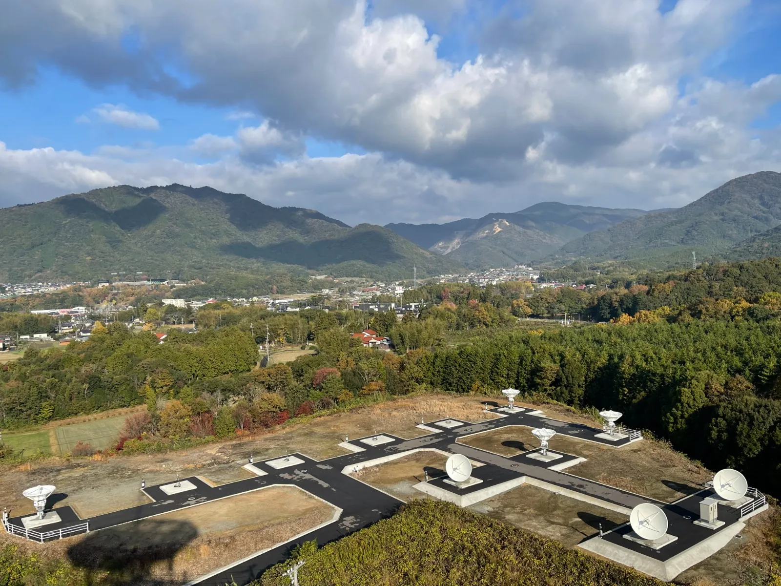 Hilltop LEO antenna farm in Asia: white dish antennas on concrete pads, with a valley town and mountains beyond