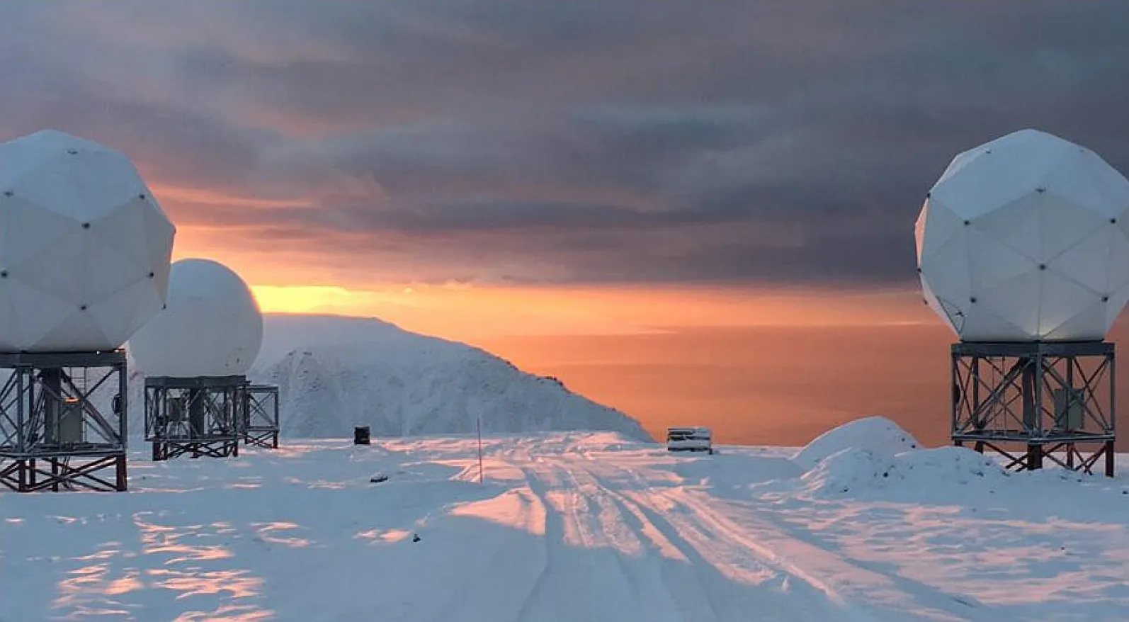 White radomes on steel frames on a snow-covered plateau in Svalbard at sunset